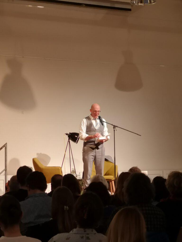 Foto von Ewald Arenz auf der Bühne bei seiner Lesung wie er gerade zum Publikum spricht.