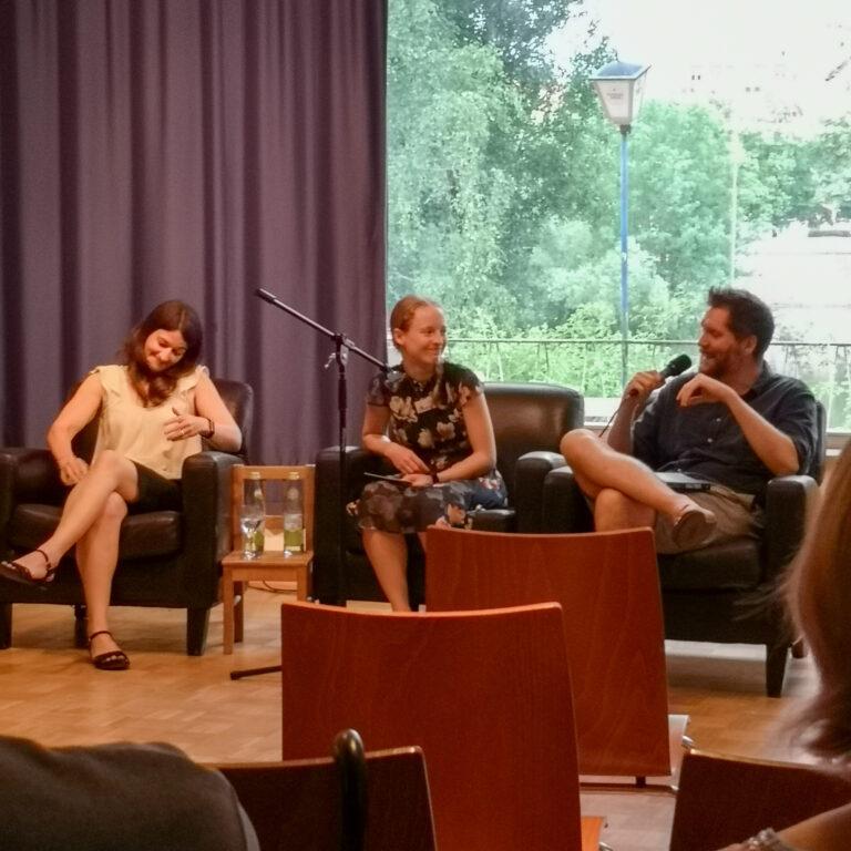 Foto der Lesung von hinten im Raum. Auf der Bühne sitzen v.l.n.r Elena Riedel, Kirsten Nähle und Johannes Maria Stangl und unterhalten sich.